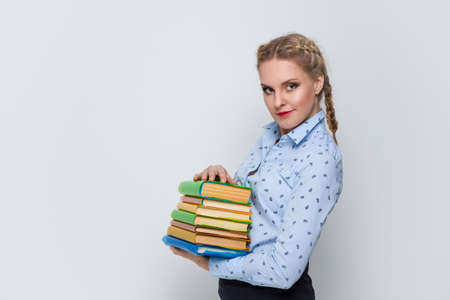 Education Concepts. Portrait of Caucasian Blond Female Posing With Heap of Books in Colorful Covers Against White.Horizontal imageの写真素材