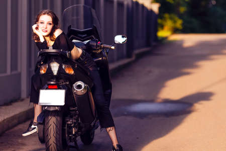 Youth Lifestyle Ideas. Young Happy Caucasian Female Biker Leaning on Sport Bike Back To Front Outdoors. Horizontal Image Compositionの写真素材