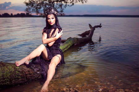 Passionate Sensual Beautiful Brunette Female In Black Dress Posing At Sea On Tree While Wearing...