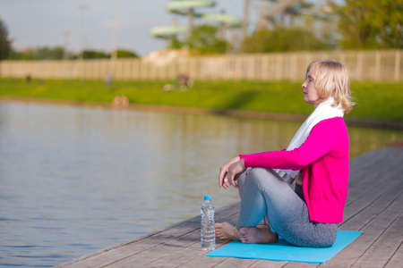 View of Mature Caucasian Blond Woman During Yoga Practice on Blue Mat At Water Shore Outdoor. Horizontal Shotの写真素材