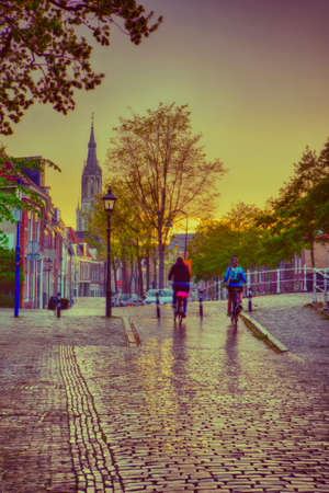 Dutch Travel Ideas. Friendly Couple in Holland Traveling on Bicycles in Old City Delft During Pouring Rain with Grey Clouds. Vertical Imageの写真素材