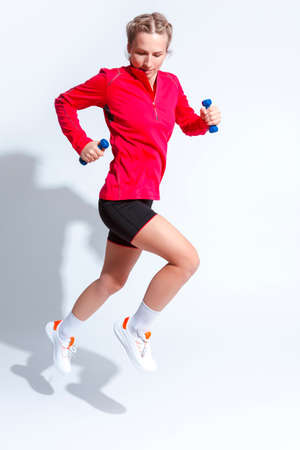 Sport Ideas. Active Caucasian Female in Red Long Sleeve Jersey And Jogging Outfit Jumping With Barbells On White. Vertical Orientationの写真素材