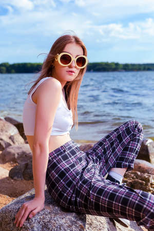 Smiling Happy Caucasian Blond Girl in Casual Clothing Throwing Stone On Sea and Posing At Shoreline...