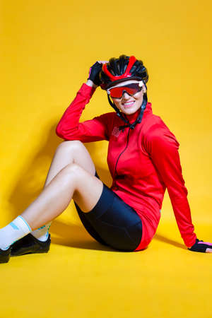 Portrait of Positive Female Road Cyclist in Professional Outfit Sitting On Floor Against Yellow Background. Vertical Imageの写真素材