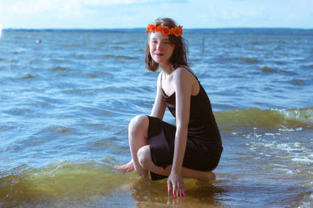 Positive Caucasian Brunette Girl in Casual Clothing Relaxing on Sea Waves While Wearing Flowery Garland In Front of Sea Shore At Daytime. Horizontal Imageの写真素材
