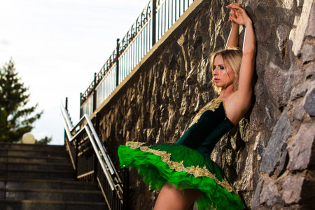 Portrait of Dancing Professional Caucasian Ballerina in Green Tutu Dress Posing Against Stony Wall Ourdoors. Horizontal Imageの写真素材