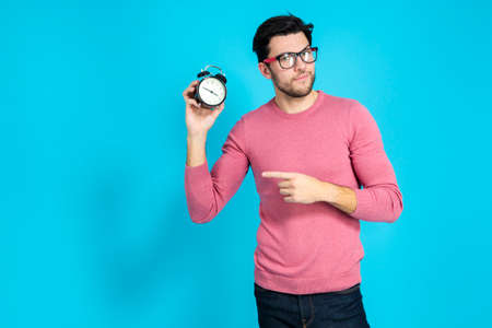 Youth LIfestyle. Portrait of Young Caucasian Man in Glasses Gesturing With Alarm Clock And Lifted Hand With Point Finger. Horizontal Image Compositionの写真素材