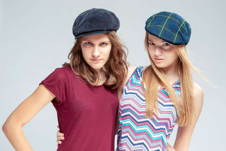 Two Serious Caucasian Girlfriends Posing Together While Wearing Caps Over White Background....