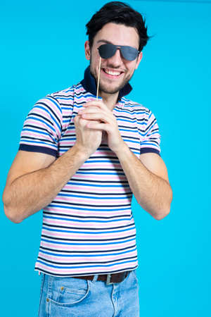 Positive Smiling Caucasian Handsome Guy Standing With Artistic Paper Glasses in Casual Clothing Against Seamless Blue Background.Vertical imageの写真素材