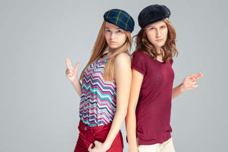 Modern Lifestyle. Two Blond Caucasian Girlfriends Posing Together While Wearing Caps Over White...