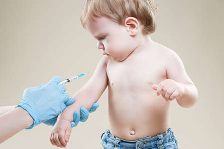 Little Sad Caucasian Boy Is Beeing Vaccinated Using Syringe Against Beige Background. Horizontal Imageの写真素材