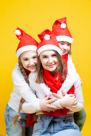 Three Positive Caucasian Girls With Santa Hats Having Fun While Embracing and Cuddling To Each Other Against Trendy Green-Blue Background. Vertical imageの写真素材