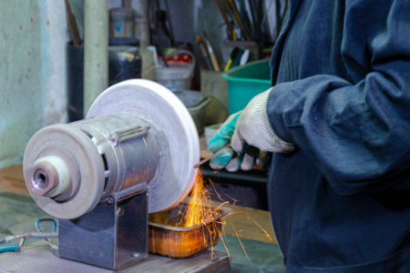 Metal Processing Concepts. Male Professional Fitter in Protective Gloves Using Gringer Tool For Metal Work With Bunch of Sparks in Workshop. Square Imageの写真素材