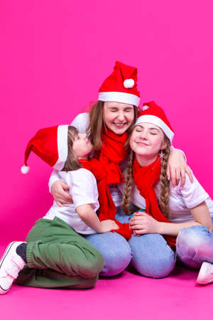 Three Positive Caucasian Girls With Santa Hats Having Fun While Embracing and Cuddling To Each Other Against Trendy Green-Blue Background. Vertical imageの写真素材