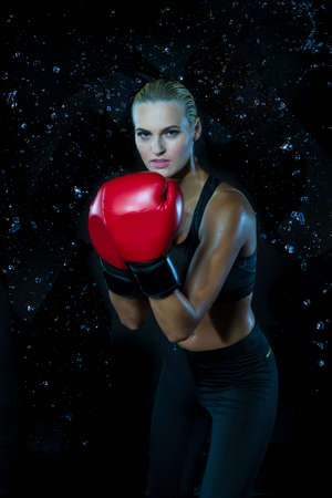 Active Female Boxer  Posing in Red Gloves And Making Hit Against Multiple Water Droplets. Vertical...