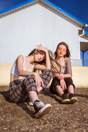 Natural Portrait of Two Relaxed Girlfriends Posing Together At Stony Wall Against Blue Sky Outdoor. Vertical Shotの写真素材