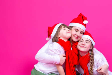 Holidays Ideas. Three Smiling Happy Caucasian Family Girls In Santa Hats Having Fun While Embracing Each Other With Hugs Over Trendy Yellow Background. Square Imageの写真素材