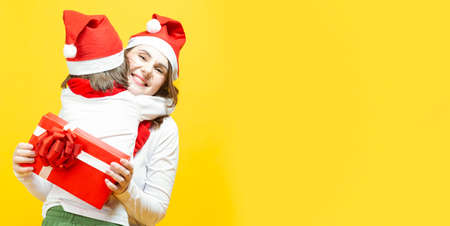 Positive Caucasian Family Couple With Mother an Young Winsome Daughter Embracing with Happy Facial Expression in Santa Hats Over Yellowの写真素材