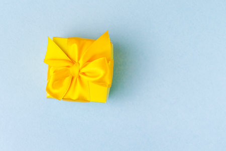 Upper Closeup View Of Wrapped Christmas and New Year Gift in Yellow Paper Tiny Box  With Ribbon Placed Over Blue Background. Horizontal Imageの写真素材