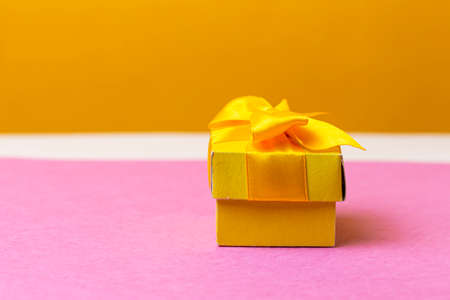 Wrapped Christmas and New Year Gift in Yellow Paper Tiny Box Placed Over Pink and Yellow Background. Horizontal Shotの写真素材