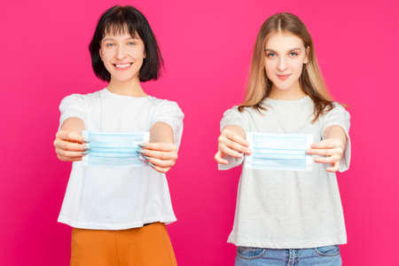 Couple of Two Positive Smiling Caucasian Girls Together Holding Cups Filled With Colorful Juice or Smoothie Having Fun Over Pink Background. Vertical Imageの写真素材