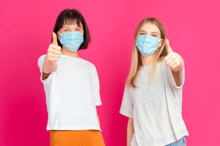 Couple of Two Positive Smiling Caucasian Girls Together Holding Cups Filled With Colorful Juice or Smoothie Having Fun Over Pink Background. Vertical Imageの写真素材