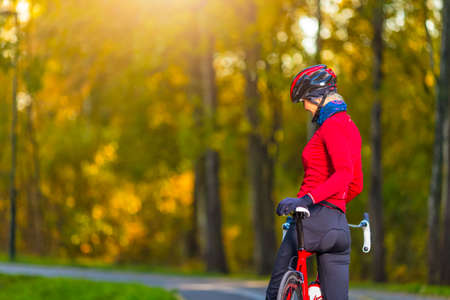 Cycling Ideas. Winsome Female Road Cyclist Posing With Modern Carbon Race Bike In Long Sleeve Cycling Outfit Against Yellow Background. Vertical Orientationの写真素材