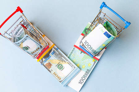 Upper View of Two Shopping Trolleys Carts With US Dollars and Euro Currency Banknotes Over Trendy...