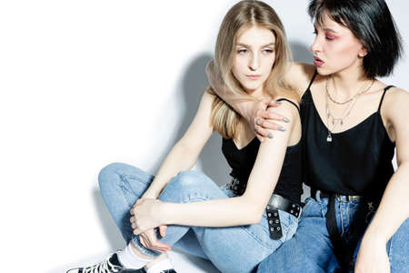 Full Length Portrait of Two Caucasian Girls Standing Embracing With Each Other in Blue Jeans Looking Straight Over White Background. Vertical Imageの写真素材