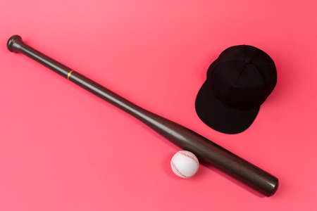 Image of Stylish Laquered Wooden Brown American Baseball Bat Placed With Clean Leather White Baseball Ball and Black Cap Over Trendy Coral Pink Background. Horizontal Imageの写真素材
