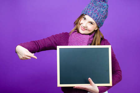 Holidays Ideas. Positive Cute Caucasian Mature Woman in Santa Hat and White Shirt Holding Wrapped Red Gift Box in Front While Pointing With Finger To Box Over Yellow. Vertical Shotの写真素材