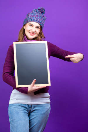 Winsome Caucasian Woman in Purple Pullover Clothing Holding and Pointing TV Remote Control To VIewew Straight Forward While Posing Over Purple Background.Vertical Imageの写真素材