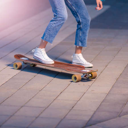 Closeup of Legs of Longboard Skater Girl Practicing on Street at Beautiful Summer Evening Outdoors.Square imageの写真素材