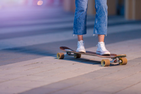 Closeup of Legs of Longboard Skater Girl Practicing on Street at Beautiful Summer Evening...