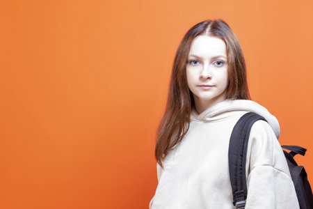 European Female Teenager Student Girl With Backpack While Holding Hands in Pockets Isolated Over Orange Background with Happy Smiling Face Standing With Confidence.Horizontal Imageの写真素材
