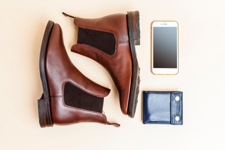 Pair of Classic Leather Chealsea Boots, Blue Leather Wallet, Cellphone Placed Near One Another On Beige Background. Horizontal imageの写真素材