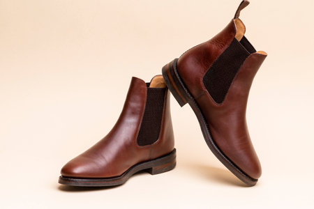 Footwear ideas. Pair of Classic Leather Chealsea Boots As Still Life Concepts Placed Over Beige...