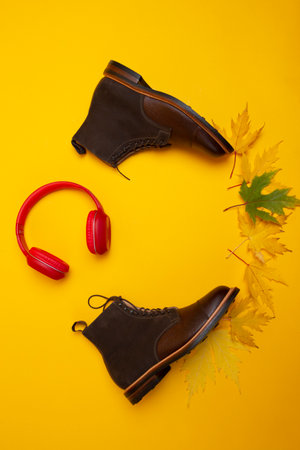 Dark Brown Grain Brogue Derby Boots Made of Calf Leather with Rubber Sole Placed With Yellow Maple Leaves and Headphones Over Yellow. Vertical Imageの写真素材