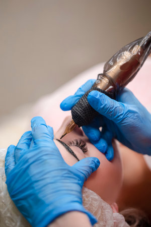 Beautiful Woman with Thick Brows in Beauty Salon While Beautician Doing Tattooing Eyebrow For Professional Makeup and Cosmetology Skincare.Vertical imageの写真素材