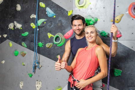Caucasian Athletes Climbing Up Together on Steep Rock climbing on artificial wall indoors As Showing Thumbs Up Sign. Horizontal Shotの写真素材