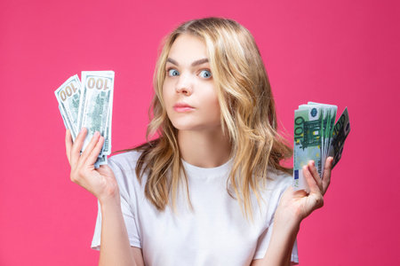 Concentrated Caucasian Girl Posing WIth Bunch of American Currency banknotes And euro While Against Coral Background. Horizontal imageの写真素材