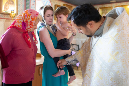 Minsk, Belarus - June 16, 2022: Baptism Ceremony of a Child While Mother Holding Kid On Arms During Anointing of Child Legsのeditorial素材