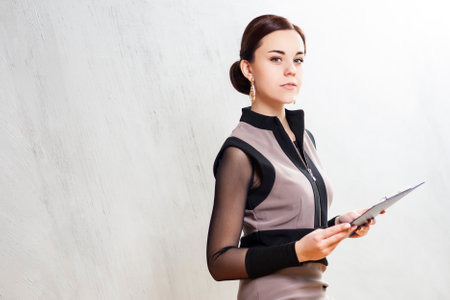 Winsome Tranquil Caucasian Entrepreneur in Dark Dress Jacket Posing With Pad Folder In Studio Against Gray.Horizontal imageの写真素材