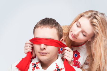 Two Loving Embraced Caucasian Couple in National Belarussian and Russian Decorated Costumes Playing With red Ribbon Blind Against White.Horizontal imageの写真素材