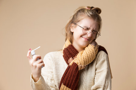 Sick Caucasian Female With Sore Throat Using Spray Inhaler for The Infection Protection and Disinfection Over Beige.Horizontal Imageの写真素材