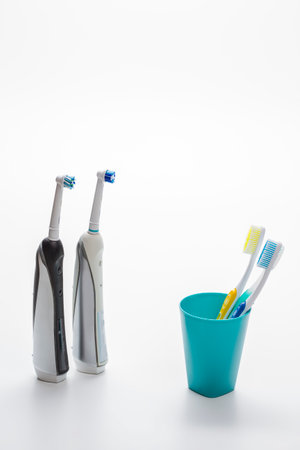 Two Professional Electric Toothbrushes In Front of Four Manual Tooth Brushes in One Cup Over White Background. Vertical imageの写真素材