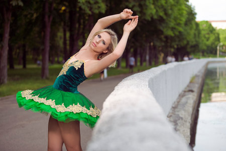 Winsome Artistic Professional Caucasian Ballet Dancer in Green Tutu Dress Posing Near River With Lifted Hands in Summer Park Outdoors. Horizontal imageの写真素材