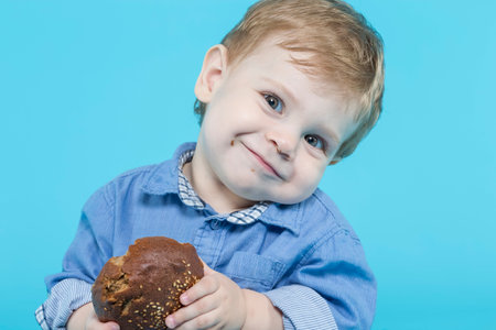 Closeup Image of One Positive Smiling Little Caucasian Child With Freshly Baked Bun Against Blue Background. Horizontal Image Orientationの写真素材