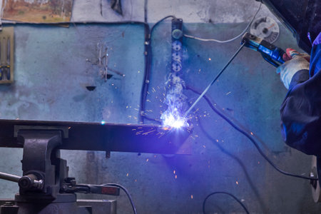 Professional Male Welder in Protective Mask During Welding Process of Metal Rod At...