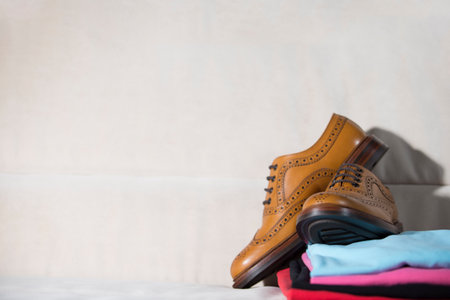 Pair of Tanned Brogue Derby Shoes of Calf Leather with Rubber Sole With Heap of Clothes On Coach. Horizontal Shotの写真素材